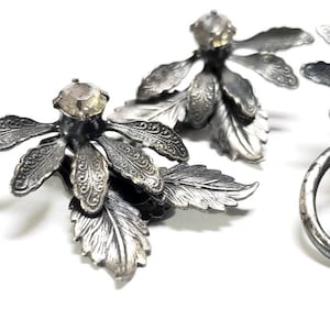 Puede incluir: Un par de pendientes de plata con un diseño floral y brillantes de cristal transparentes. Los pendientes están hechos de metal y tienen un diseño delicado e intrincado.