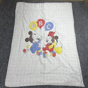 May include: A white rectangular baby quilt featuring a repeating pattern of small red and blue diamond shapes. The center graphic displays Mickey Mouse and Minnie Mouse with Pluto, holding balloons labeled A, B, and C, alongside alphabet blocks.