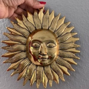 May include: A gold-colored metal sun wall decor with a face and rays.