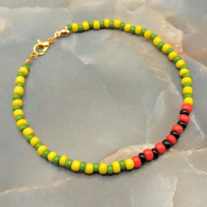 Può includere: Un braccialetto di perline con perline gialle, verdi, rosse e nere. Il braccialetto ha una chiusura color oro. Le perline sono infilate per formare un accessorio colorato.