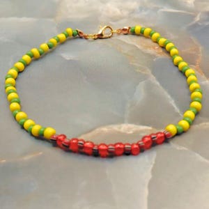 May include: A colourful beaded bracelet with yellow, green, and red beads. The bracelet has a gold-coloured clasp. The beads are small and round, creating a vibrant accessory.