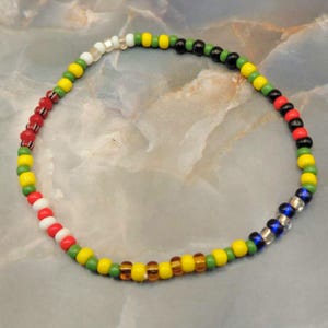 May include: A beaded bracelet with a colorful design. The bracelet features a variety of small, round beads in colors including red, yellow, green, black, white, blue, and silver. The beads are strung together to form a flexible band.