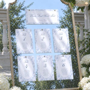 May include: A gold-framed mirror displays a seating chart for a wedding. The chart features six cards with guest names, and a header that reads "Please Find Your Seat." The cards have a blue floral design.