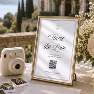 Peut inclure: Un panneau encadré d'or avec du papier blanc portant le texte Share the Love, un code QR et les noms Madeleine & Frederick, May 21, 20XX. À côté se trouvent un appareil photo instantané blanc et deux petites photos imprimées sur une surface claire.
