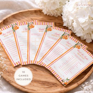 Puede incluir: Un conjunto de tarjetas de juegos para despedida de soltera con detalles en naranja y rosa. Cada tarjeta presenta un juego diferente, como "Bridal Bingo" y "Would She Rather?" Las tarjetas están dispuestas sobre una bandeja de madera con decoraciones florales.