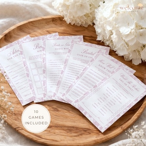 May include: A collection of bridal shower game cards with floral borders and various game titles, including "Advice for the Bride" and "Would She Rather." The cards are arranged on a wooden tray, with a "10 Games Included" sticker.