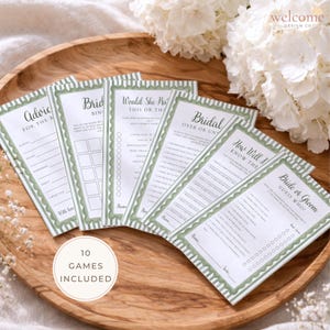 May include: A collection of ten bridal shower game cards with green and white decorative borders. The cards are arranged on a wooden tray, with text such as "Advice for the Bride" and "Bride or Groom". A white floral arrangement is in the background.