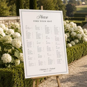 May include: A white wedding seating chart sign on a wooden easel featuring black text that reads Please FIND YOUR SEAT, a list of names organized alphabetically by letter, and the names Madeleine & Frederick with the date MAY 21, 20XX.