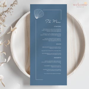Op de afbeelding: Een blauwe menukaart met een schelpmotief en de tekst "The Menu". De kaart bevat voorgerechten, hoofdgerechten en desserts, zoals gebakken sint-jakobsschelpen en gegrilde tonijn. De kaart ligt op een houten bord.