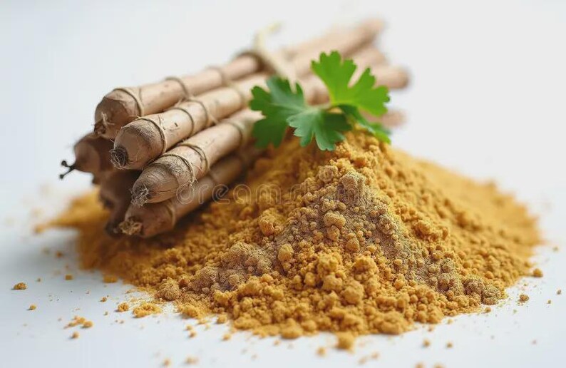 May include: A bundle of turmeric roots tied with string, next to a mound of vibrant yellow turmeric powder. A green leaf is placed on the powder. The background is white.