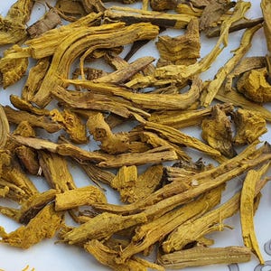 May include: Close-up of dried, yellow-orange root pieces. The pieces vary in size and shape, with a rough, textured appearance. The image shows a collection of these dried roots, likely for herbal or culinary use.