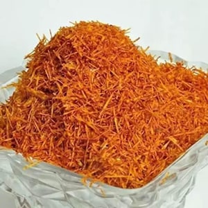May include: A close-up shot of a pile of saffron threads, a vibrant orange-red spice, filling a clear, decorative glass bowl. The threads are finely cut and appear dry. The bowl has a textured, faceted design.