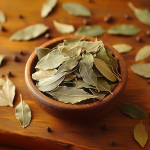 May include: A wooden bowl filled with dried bay leaves, surrounded by scattered leaves and peppercorns. The leaves are a muted green color, and the bowl is a warm brown. The image is shot from above, showcasing the natural textures and colors.