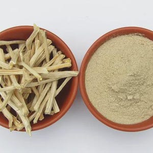 May include: Two terracotta bowls on a white surface. One bowl contains light-coloured, dried, stick-like pieces. The other bowl holds a fine, light-brown powder. The items are likely ingredients for cooking or herbal remedies.