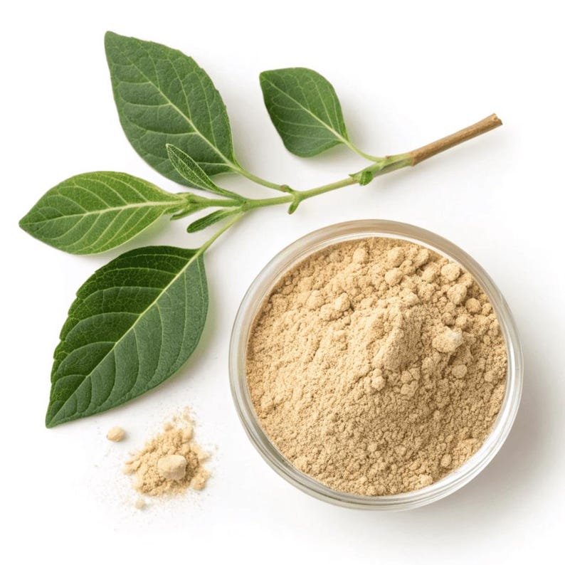 May include: A top-down view of a glass bowl filled with light brown powder, with a small pile of the same powder next to it. A green leafy sprig is positioned above the bowl, with the leaves and stem visible. The background is white.