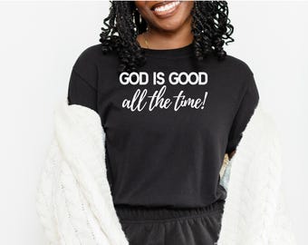 Pode incluir: T-shirt preto com gola redonda com o texto branco "GOD IS GOOD all the time!". A camisa é combinada com calças de moletom pretas e um cardigan branco de malha.
