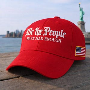 以下が含まれることがあります： 「We the People HAVE HAD ENOUGH」の白文字が特徴的な赤いベースボールキャップ。キャップの側面にはアメリカ国旗のパッチが付いています。背景には自由の女神が見えます。