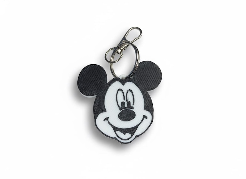 May include: A black and white Mickey Mouse keychain with a silver clasp. The keychain features a smiling Mickey Mouse face with large black ears and a white face. The design is simple and iconic.
