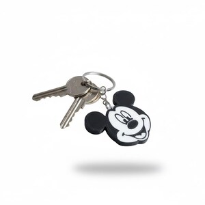 May include: A Mickey Mouse keychain with a black and white design, attached to a silver key ring with two keys. The keychain features a smiling Mickey Mouse face.