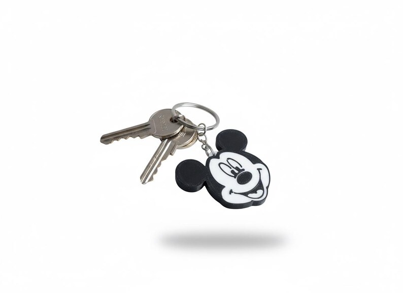May include: A Mickey Mouse keychain with a black and white design, attached to a silver key ring with two keys. The keychain features a smiling Mickey Mouse face.