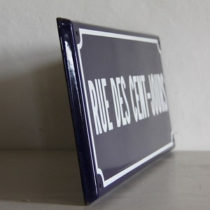 May include: A blue and white enamel street sign with the text "RUE DES CENT-JOURS" in white lettering.