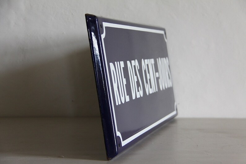 May include: A blue and white enamel street sign with the text "RUE DES CENT-JOURS" in white lettering.