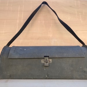 May include: A vintage metal toolbox with a black leather strap and a metal latch. The toolbox is green and has a worn, distressed look.