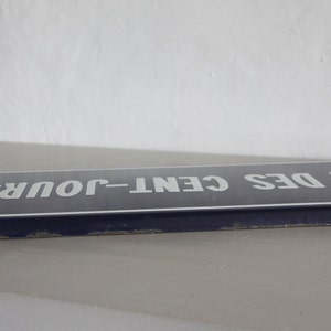 May include: A blue enamel street sign with white lettering that reads "RUE DES CENT-JOURS".