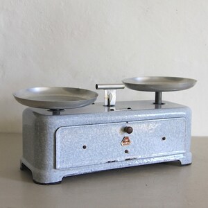 May include: A vintage blue kitchen scale with two silver metal bowls. The scale has a white label with the word "WAAGE" printed on it.