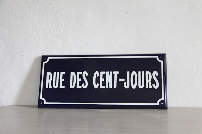 May include: A blue and white enamel street sign with the text "RUE DES CENT-JOURS" in white lettering.