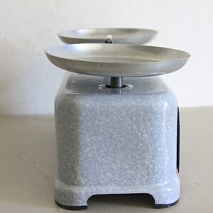 May include: A vintage, gray, metal kitchen scale with two round, silver weighing pans. The scale has a speckled, gray finish.