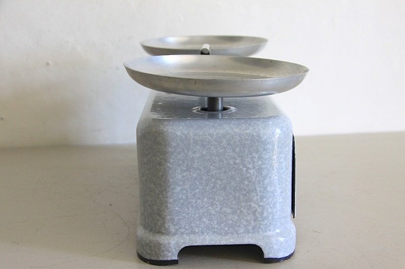 May include: A vintage, gray, metal kitchen scale with two round, silver weighing pans. The scale has a speckled, gray finish.