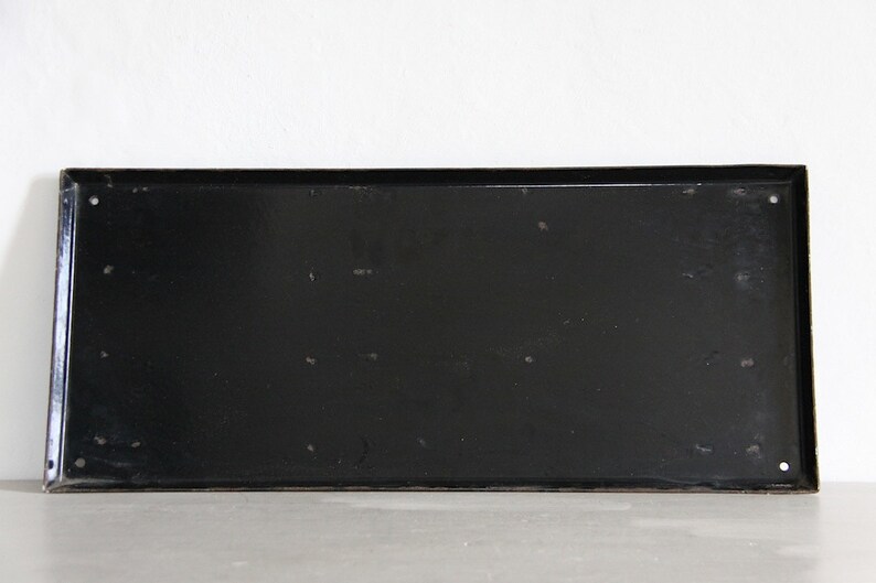 May include: A black metal rectangular sign with rounded corners. The sign is blank and has several small holes around the edges.