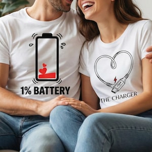 May include: White t-shirts with matching graphics. One shirt features a battery graphic with the text "1% BATTERY". The other shirt has a heart-shaped cable with a charging plug and the text "THE CHARGER".