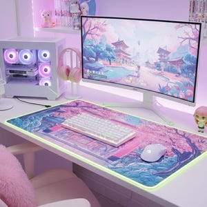 May include: A white desk setup featuring a curved monitor showing a landscape. Includes a white keyboard, mouse, and a colourful mousepad. A white computer case with illuminated fans and pink headphones are also visible.