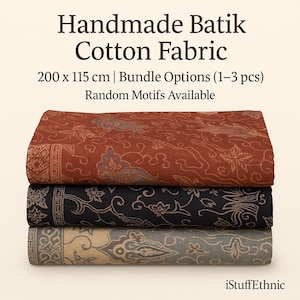 Op de afbeelding: Een stapel van drie handgemaakte batik katoenen stoffen. De bovenste stof is roodbruin met een bloemenpatroon. De middelste stof is zwart met een bloemenontwerp en de onderste stof is grijs met een bloemenpatroon. De tekst luidt "Handmade Batik Cotton Fabric".