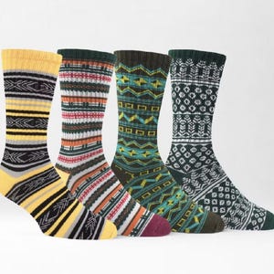 Könnte beinhalten: Vier wadenhohe Socken mit unterschiedlichen Strickmustern. Die erste ist gelb mit schwarzen und grauen Streifen. Die zweite hat rote, weiße und schwarze Querstreifen. Die dritte ist dunkelgrün mit gelben geometrischen Formen. Die vierte ist dunkelgrün mit weißen blumenartigen Motiven.