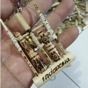 Könnte beinhalten: Ein handgefertigter Schlüsselanhänger mit einem Miniatur-Angklung-Musikinstrument aus Bambus. Der Schlüsselanhänger hat einen silbernen Metallring und das Wort "Indonesia" ist auf der Basis geschrieben. Die Bambusstücke sind mit aufwendigen Mustern verziert.
