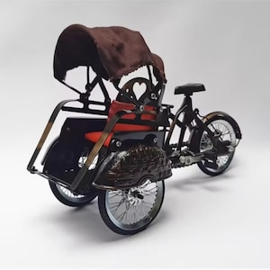 Puede incluir: Modelo en miniatura de rickshaw negro y marrón con capota marrón y asiento rojo. El modelo presenta dos ruedas traseras y una delantera, con detalles intrincados en la carrocería y las ruedas.