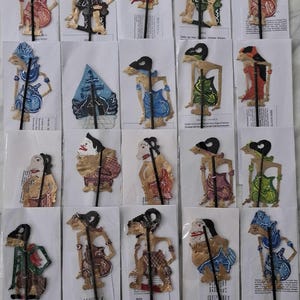 Puede incluir: Colección de marionetas de sombras Wayang Kulit indonesias. Cada marioneta presenta diseños intrincados y colores vibrantes, incluyendo rojo, azul, verde y dorado. Las marionetas están montadas en palos negros.