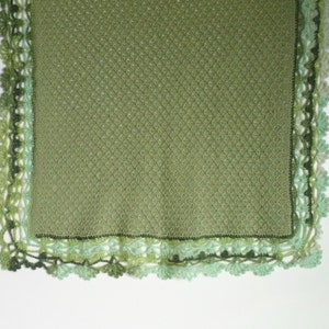 May include: A green crocheted blanket with a delicate lace border. The blanket is made with a textured stitch and has a subtle ombre effect in the border.