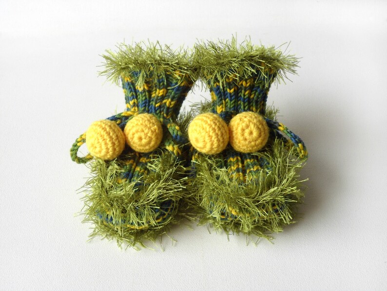 May include: A pair of green and yellow knitted baby booties with yellow pom-poms.