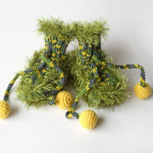 May include: A pair of green and yellow knitted baby booties with fuzzy trim and yellow pom-poms attached to the laces.