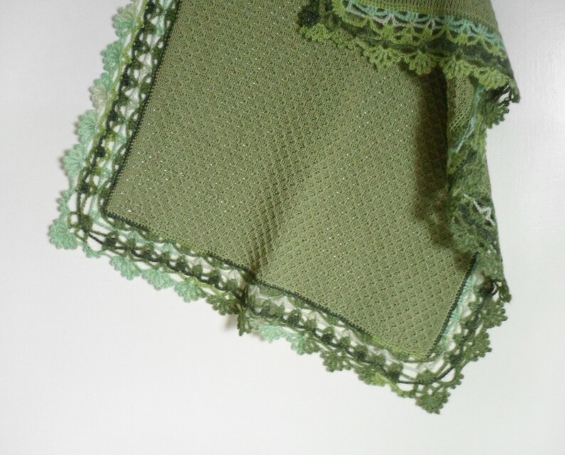 May include: A green crocheted baby blanket with a delicate lace border. The blanket is made with a soft, lightweight yarn and is perfect for cuddling.