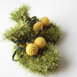 May include: A pair of green knitted baby booties with yellow pom-poms. The booties are made with a fuzzy yarn and have a plaid pattern.