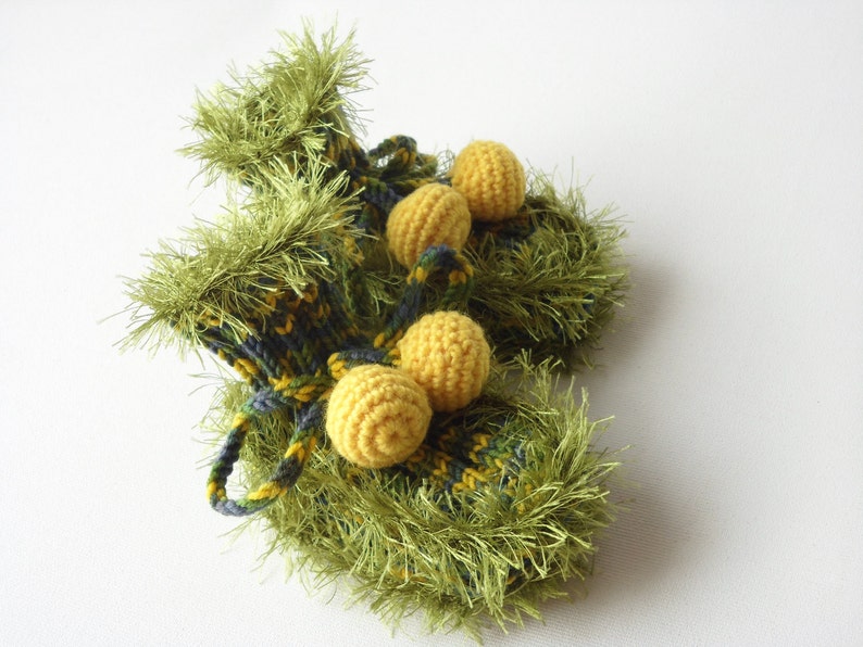 May include: A pair of green knitted baby booties with yellow pom-poms. The booties are made with a fuzzy yarn and have a plaid pattern.