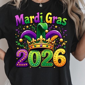 May include: Black t-shirt with a colorful Mardi Gras design. The graphic includes the words "Mardi Gras" in purple and green, a jester hat, a gold crown, and the year "2026" in green and gold.