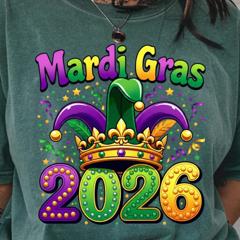 May include: Green sweatshirt with a colorful Mardi Gras graphic. The design features the words "Mardi Gras" in purple and yellow, a jester hat, a gold crown, and the year "2026" in purple, green, and gold. Confetti and streamers complete the festive look.