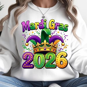 May include: White sweatshirt with a colorful Mardi Gras design. The graphic includes the words "Mardi Gras" in purple and yellow, a jester hat, a gold crown, and the year "2026" in green and gold.