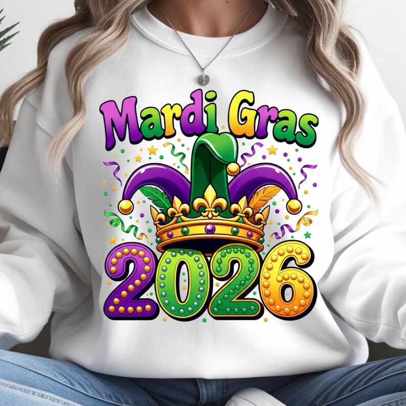 May include: White sweatshirt with a colorful Mardi Gras design. The graphic includes the words "Mardi Gras" in purple and yellow, a jester hat, a gold crown, and the year "2026" in green and gold.